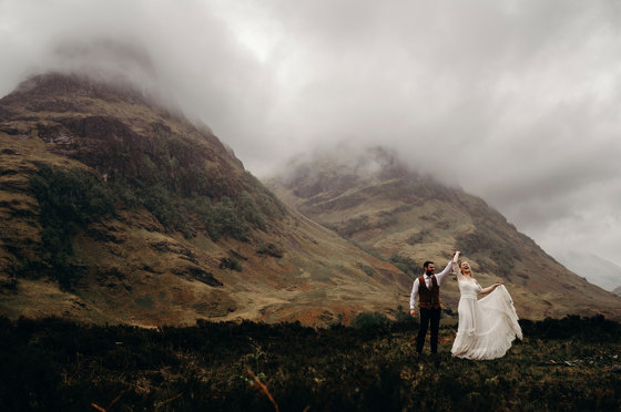 Bride and groom dancing in dramatic misty Scottish Highlands